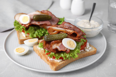 Tasty sandwiches with bacon and quail eggs served on light grey table