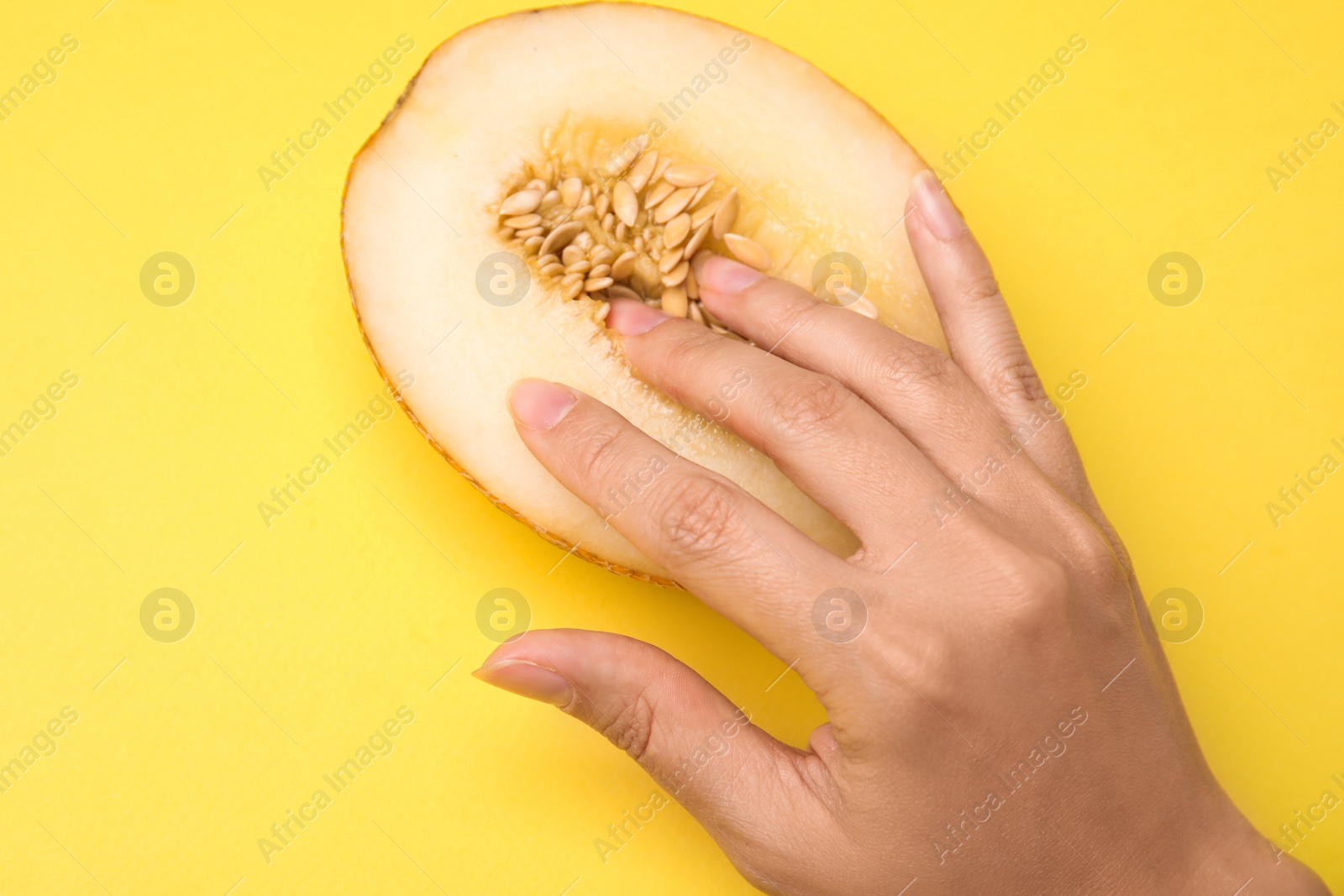 Photo of Young woman touching half of melon on yellow background, above view. Sex concept