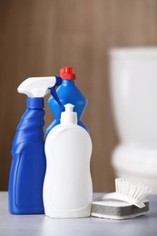 Photo of Bottles, sponge and toilet brush on table indoors. Cleaning supplies