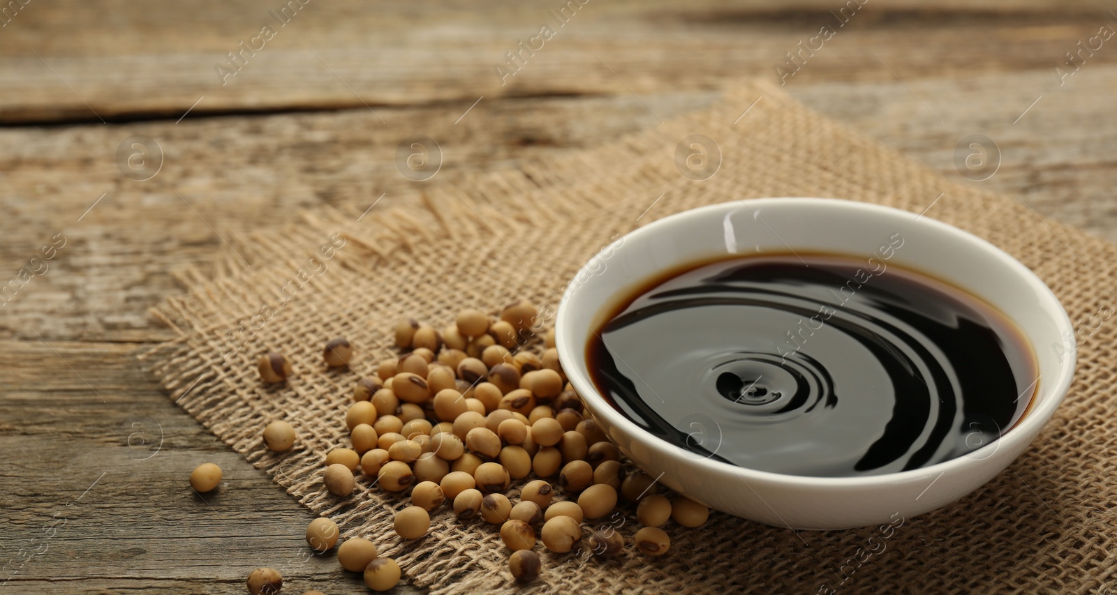 Photo of Soy sauce in bowl and beans on wooden table, closeup. Space for text