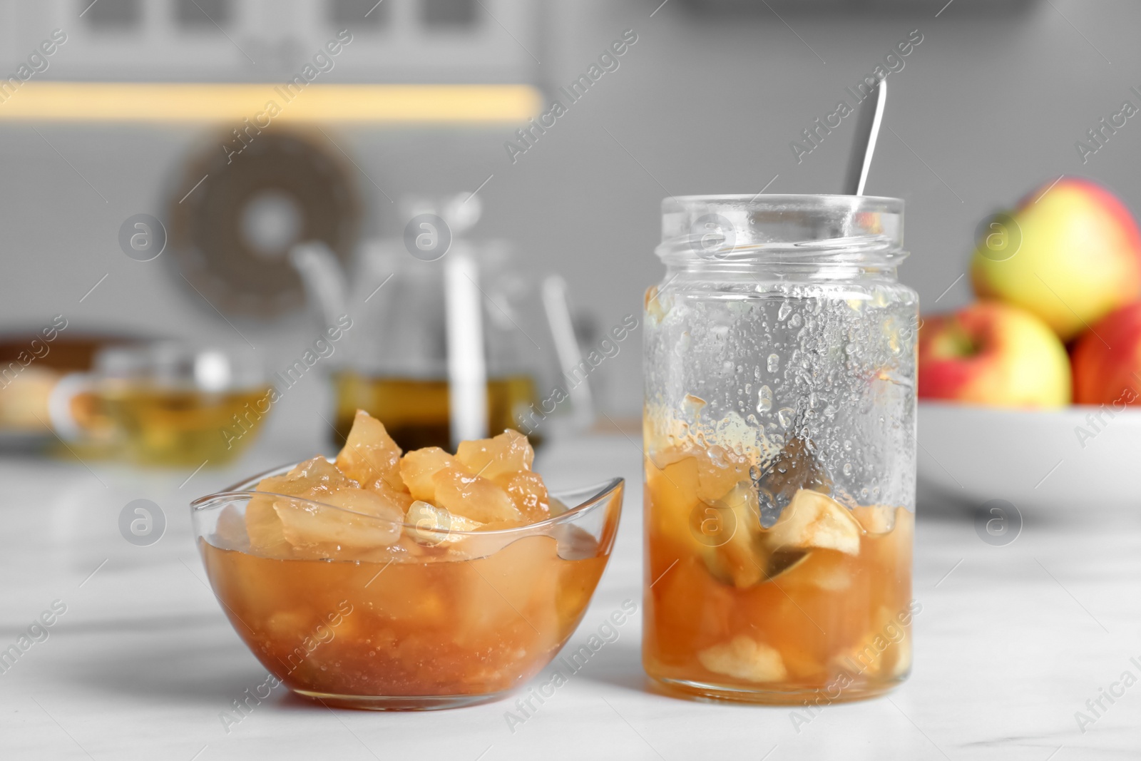 Photo of Delicious apple jam in jar and bowl on white table