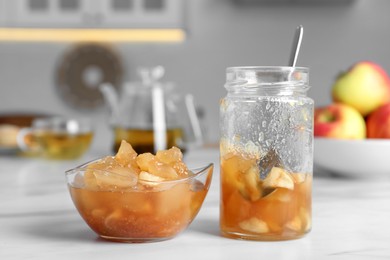 Delicious apple jam in jar and bowl on white table