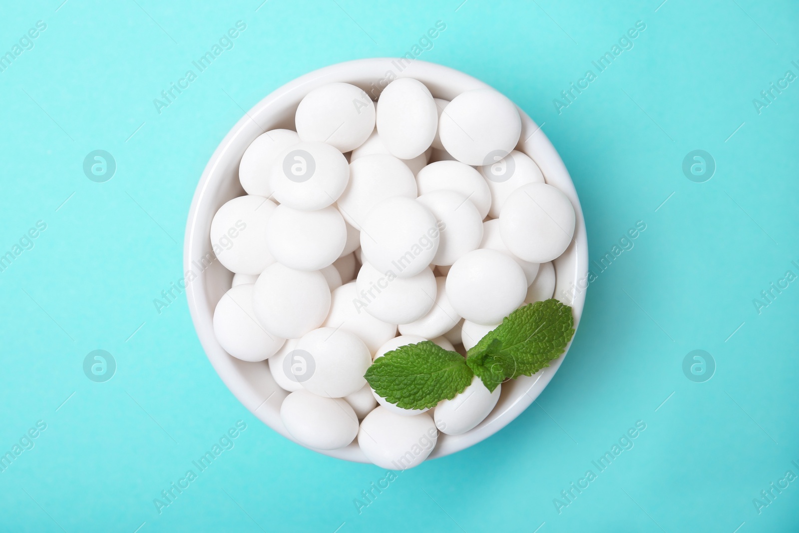 Photo of Bowl with tasty mint candies and leaves on color background, top view