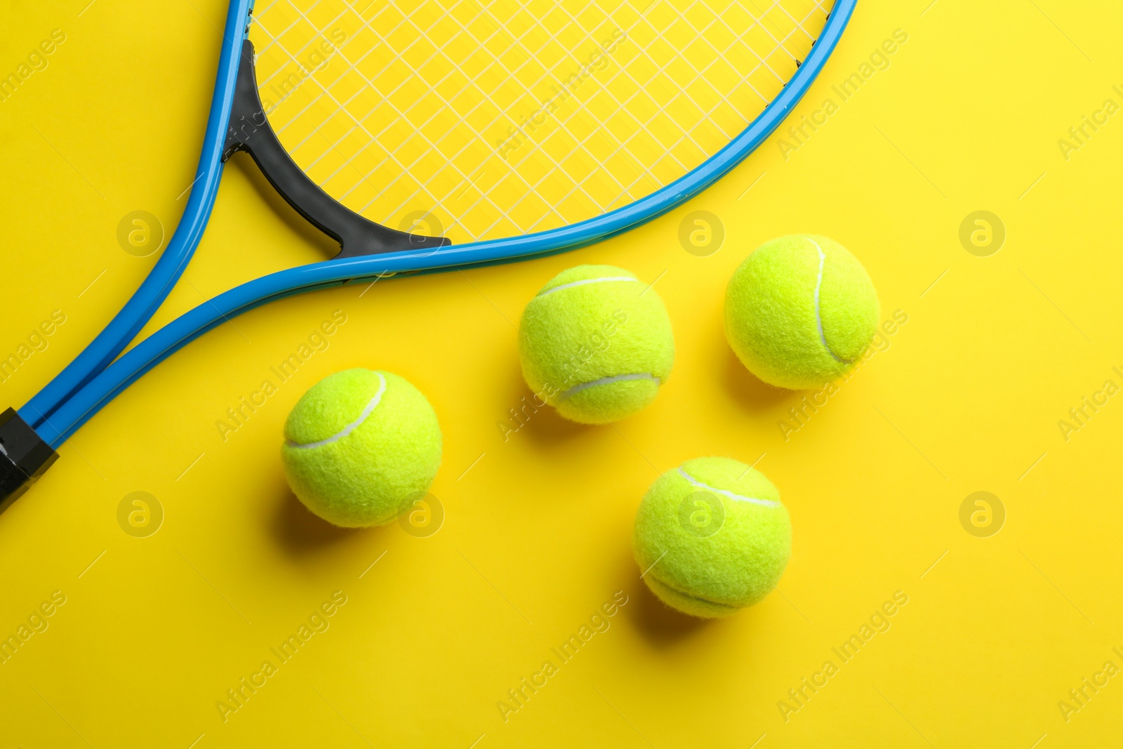 Photo of Tennis racket and balls on yellow background, flat lay. Sports equipment