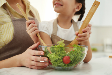 Photo of Mother and daughter cooking salad together in kitchen, closeup