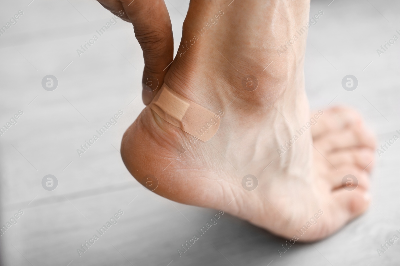 Photo of Man applying adhesive bandage on heel indoors, closeup