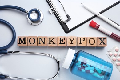 Photo of Word Monkeypox made of wooden cubes, pills and stethoscope on light background, flat lay