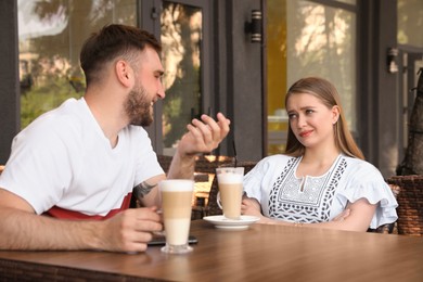 Photo of Young woman having boring date with talkative guy in outdoor cafe