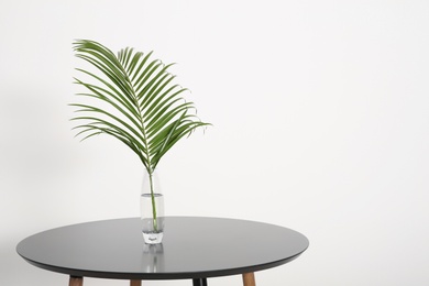 Photo of Tropical leaf in glass vase on table indoors. Idea for modern stylish interior