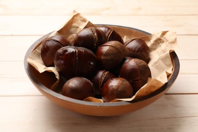 Photo of Roasted edible sweet chestnuts in bowl on wooden table, closeup