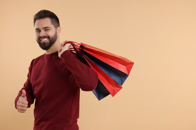 Photo of Smiling man with many paper shopping bags showing thumb up on beige background. Space for text