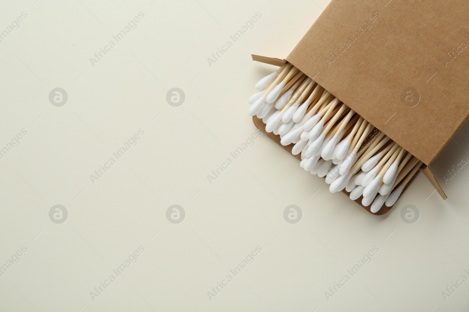 Photo of Box with wooden cotton buds on beige background, top view. Space for text