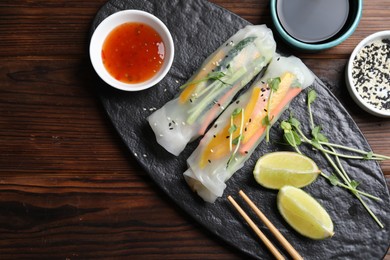 Photo of Tasty spring rolls, sauce, lime, sesame seeds and microgreens on wooden table, top view