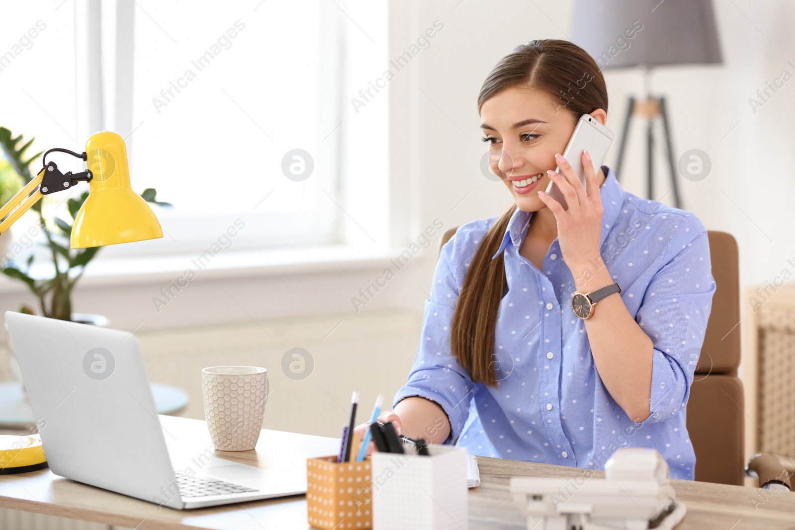 Photo of Young woman talking on phone at workplace