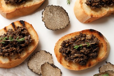 Delicious bruschettas with truffle sauce and thyme on white table, flat lay