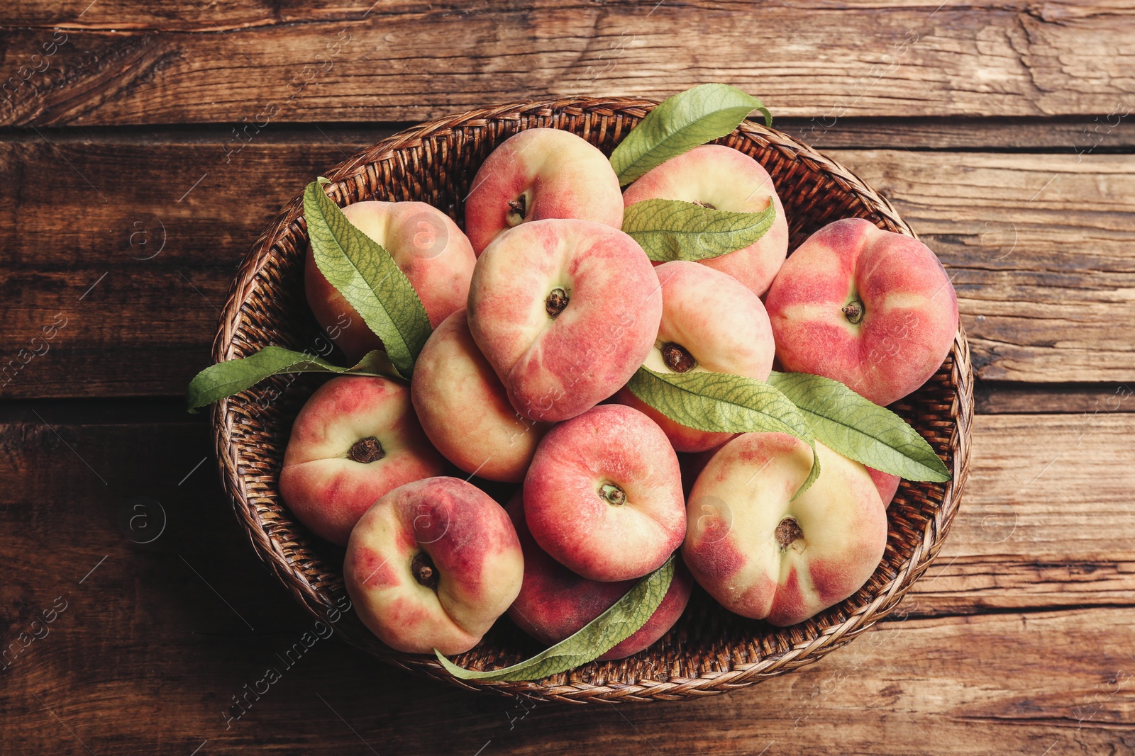 Photo of Fresh ripe donut peaches in basket on wooden table, top view