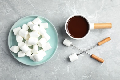 Photo of Fondue pot with dark chocolate and marshmallows on marble table, flat lay