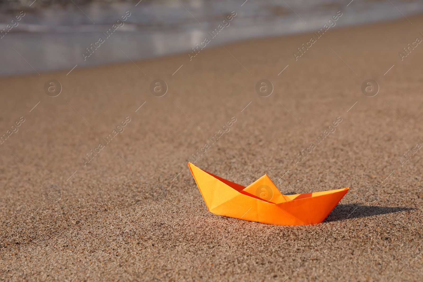 Photo of Orange paper boat on sand near sea, space for text