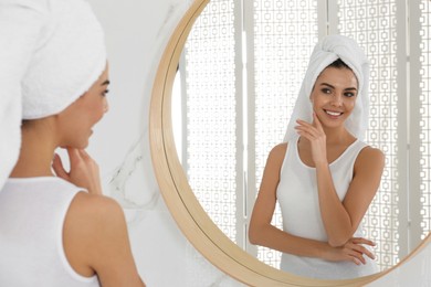 Photo of Happy young woman with clean skin looking at mirror in bathroom