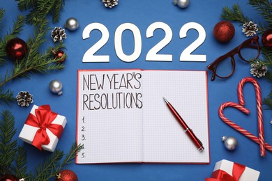 Photo of Making New Year's resolutions. Flat lay composition with notebook, 2022 numbers and festive decor on blue background
