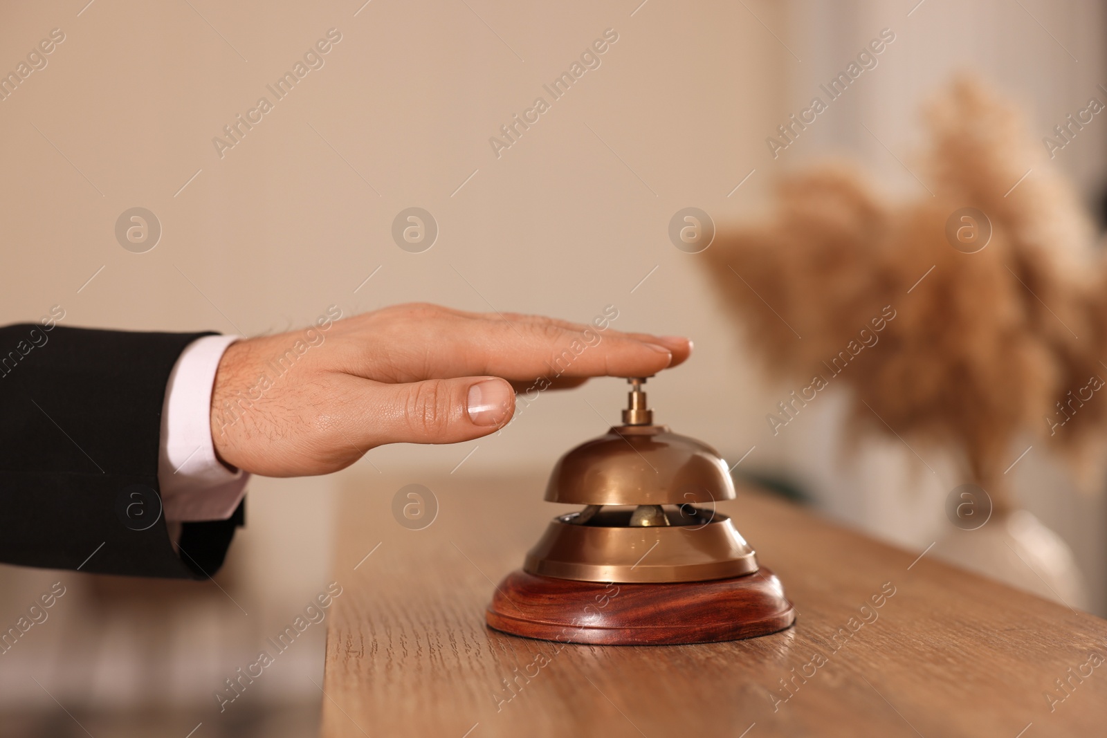 Photo of Man ringing service bell at wooden reception desk in hotel, closeup