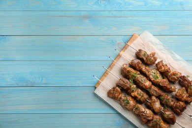 Photo of Metal skewers with delicious meat served on light blue wooden table, top view. Space for text