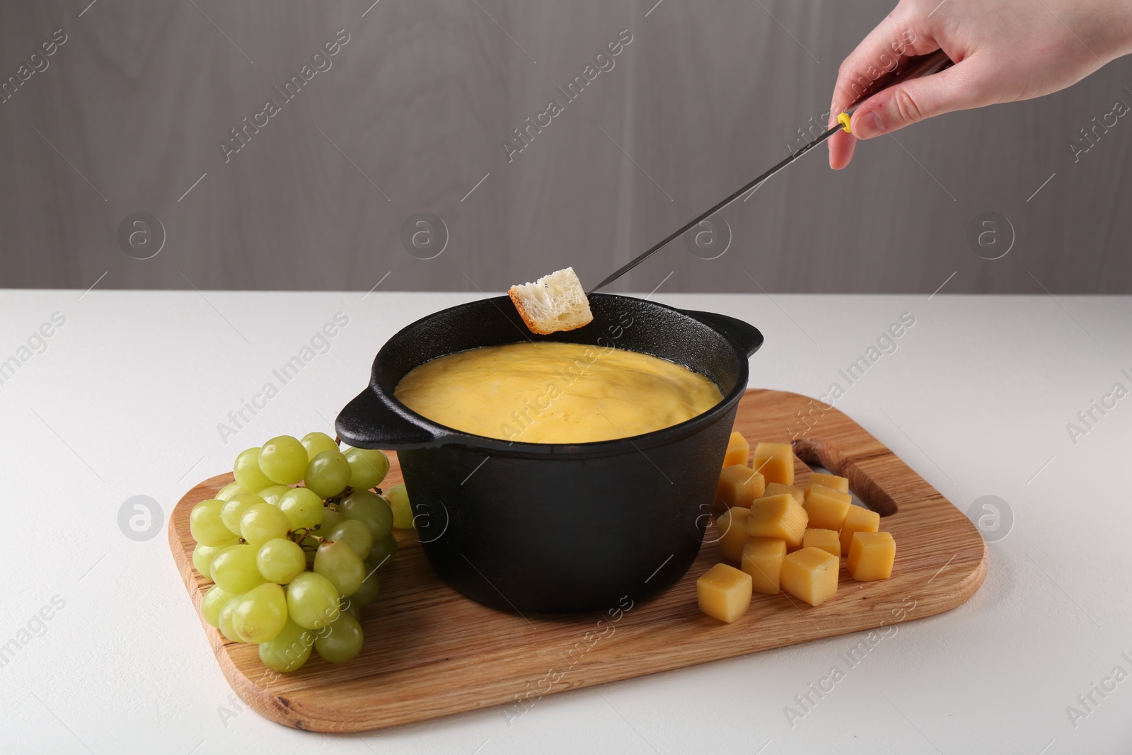 Photo of Woman dipping piece of bread into fondue pot with tasty melted cheese at white table, closeup