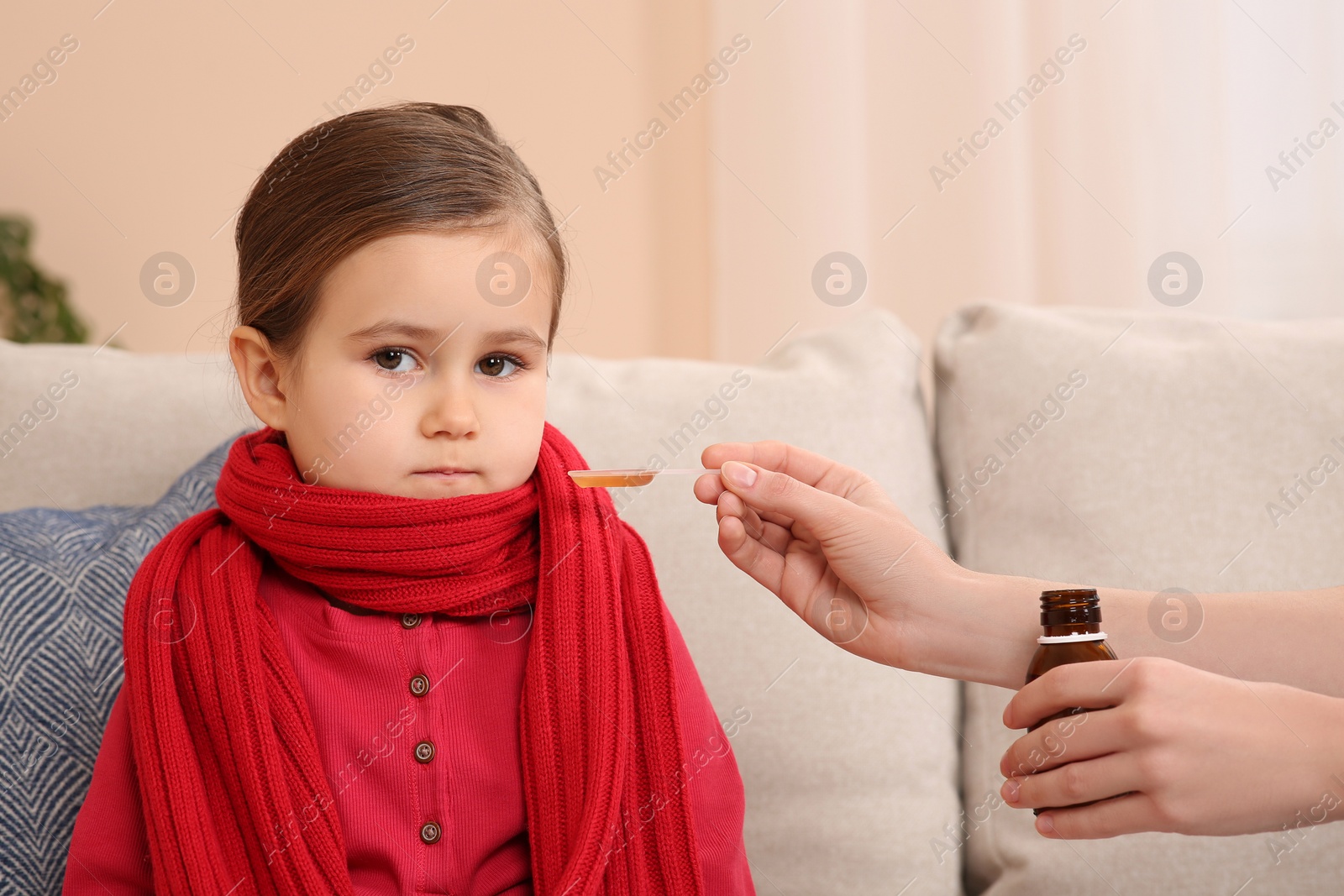 Photo of Mother giving cough syrup to her daughter on sofa indoors
