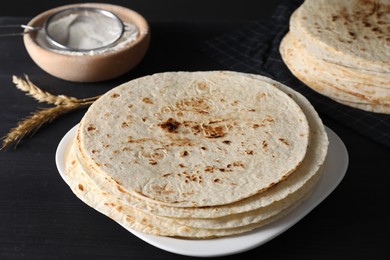 Photo of Many tasty homemade tortillas on black wooden table