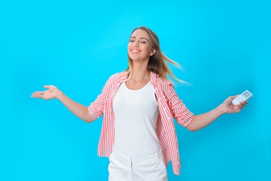 Photo of Young woman with air conditioner remote on blue background
