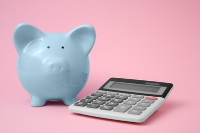 Photo of Piggy bank and calculator on pink background