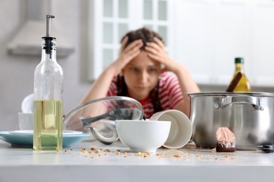 Photo of Stressed woman in messy kitchen. Many dirty dishware and utensils on table, selective focus