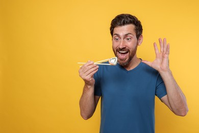 Photo of Emotional man holding sushi roll with chopsticks on orange background. Space for text