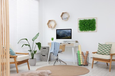 Photo of Green artificial plant wall panel and desk with computer in light room. Interior design