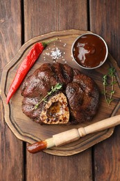 Photo of Delicious roasted beef meat served with sauce and spices on wooden table, top view