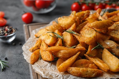 Photo of Wooden board with baked potatoes and rosemary on table, closeup