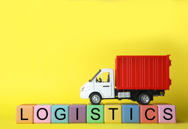 Photo of Toy truck and cubes with word LOGISTICS on yellow background, space for text. Wholesale concept