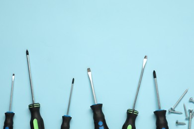 Photo of Set of screwdrivers and screws on light blue background, flat lay. Space for text