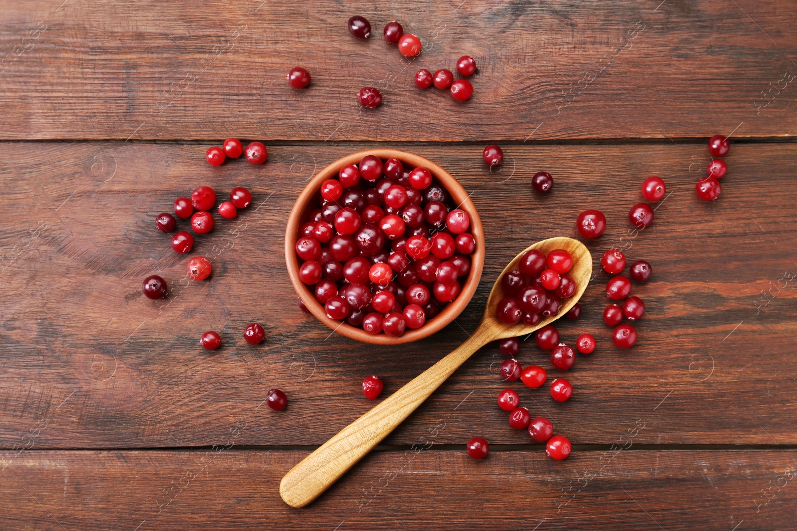 Fresh ripe cranberries in bowl and spoon on wooden table, flat lay Photo of Fresh ripe cranberries in bowl and spoon on wooden table, flat lay