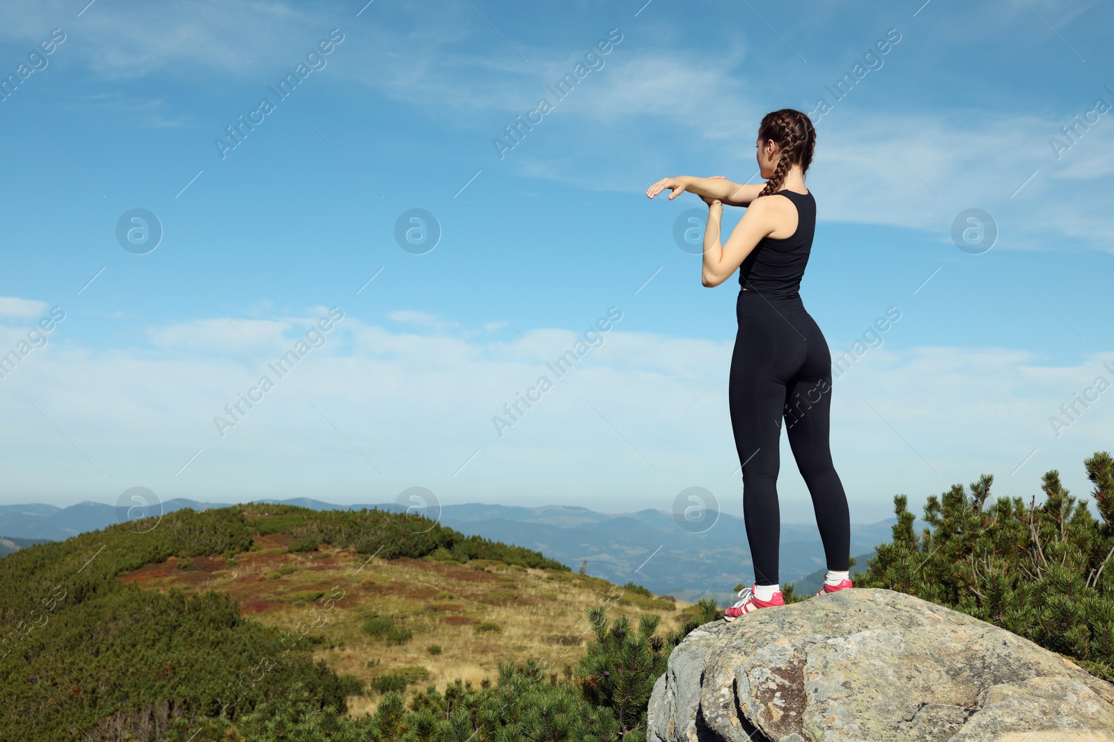 Photo of Beautiful young woman stretching on rock in mountains