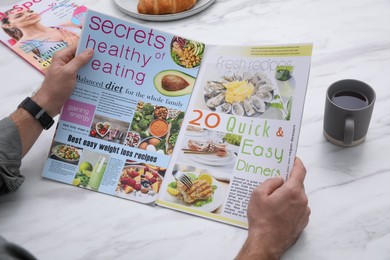 Photo of Man reading magazine during breakfast at white marble table, closeup