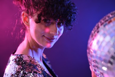 Photo of Beautiful young woman with disco ball posing on color background in neon lights