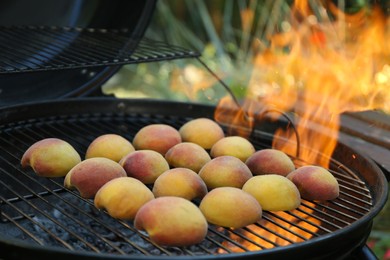 Photo of Modern grill with tasty juicy peaches and flame outdoors, closeup