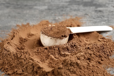 Photo of Pile of chocolate protein powder and scoop on grey table, closeup