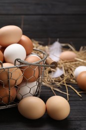 Photo of Fresh chicken eggs and dried straw on black wooden table