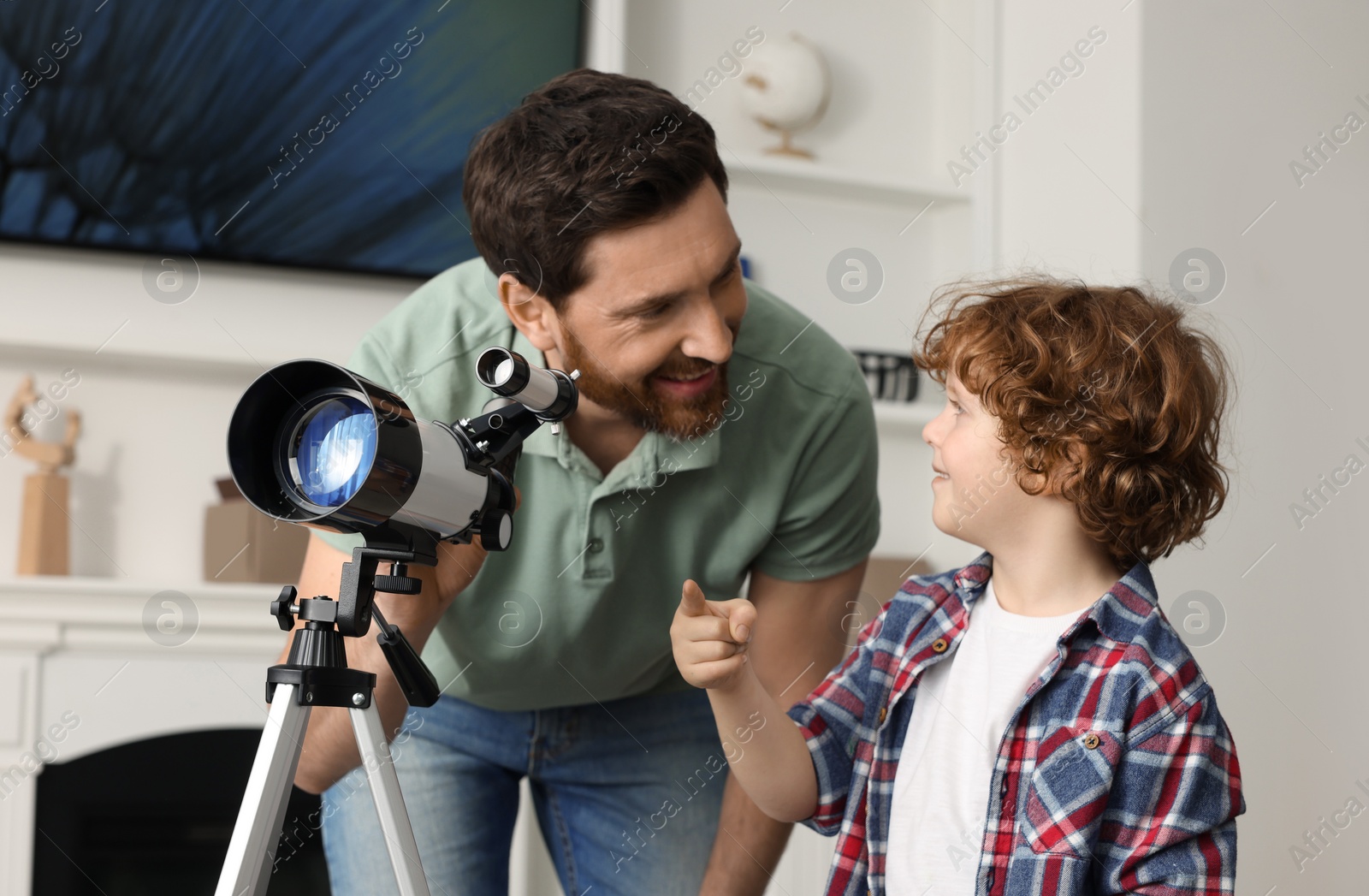 Photo of Little boy with his father using telescope to look at stars in room