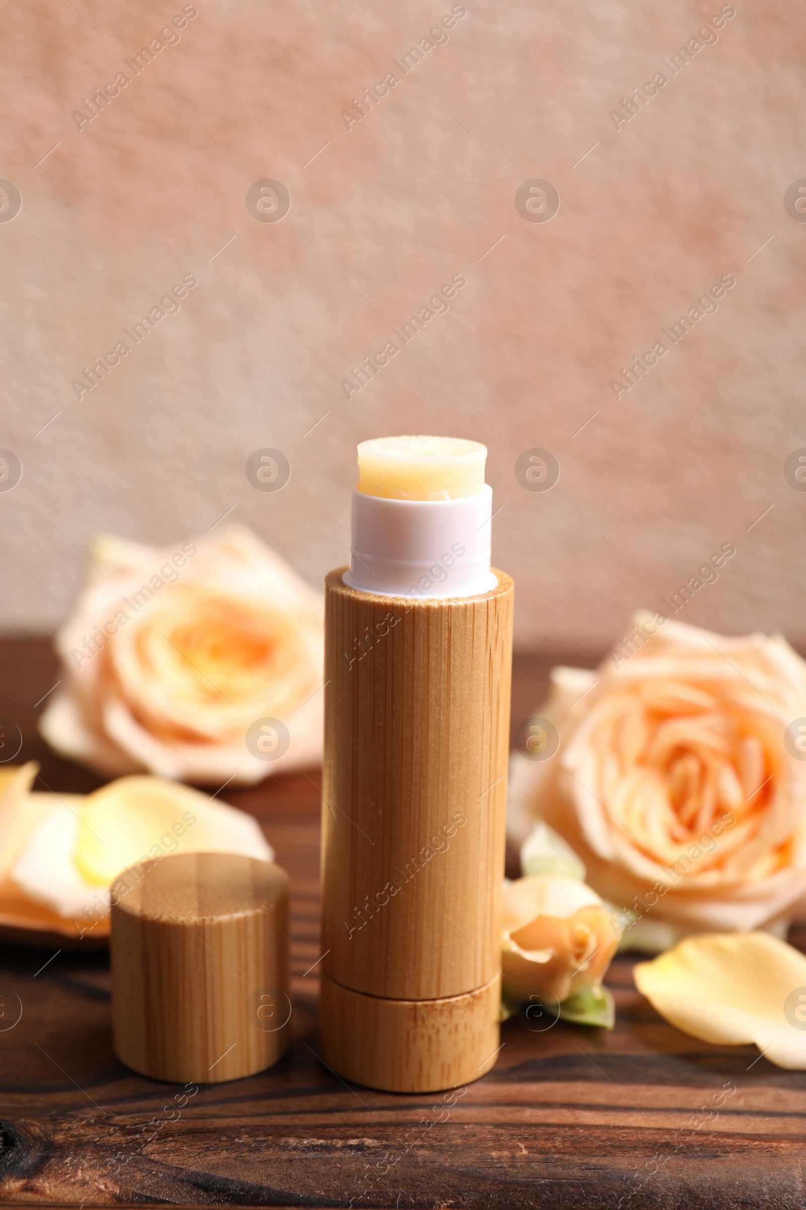 Photo of Lip balm and rose flowers on wooden table, closeup