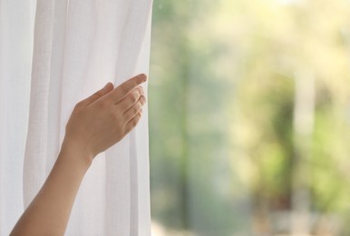 Photo of Woman opening white window curtains in room, closeup. Space for text