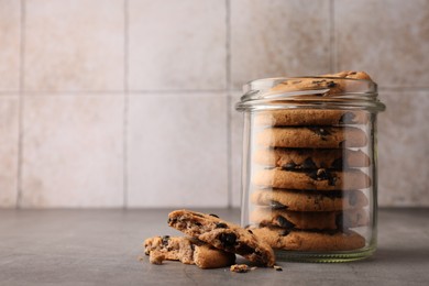Photo of Glass jar with delicious chocolate chip cookies on grey table. Space for text