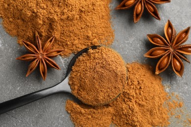 Photo of Spoon with cinnamon powder and star anise on grey table, flat lay